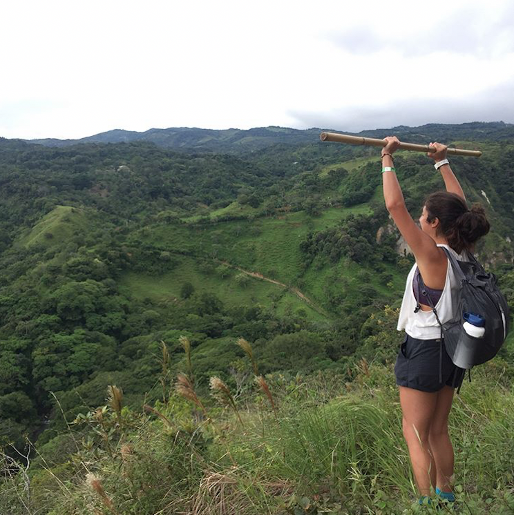 Student stands on top of hill with hands raised.