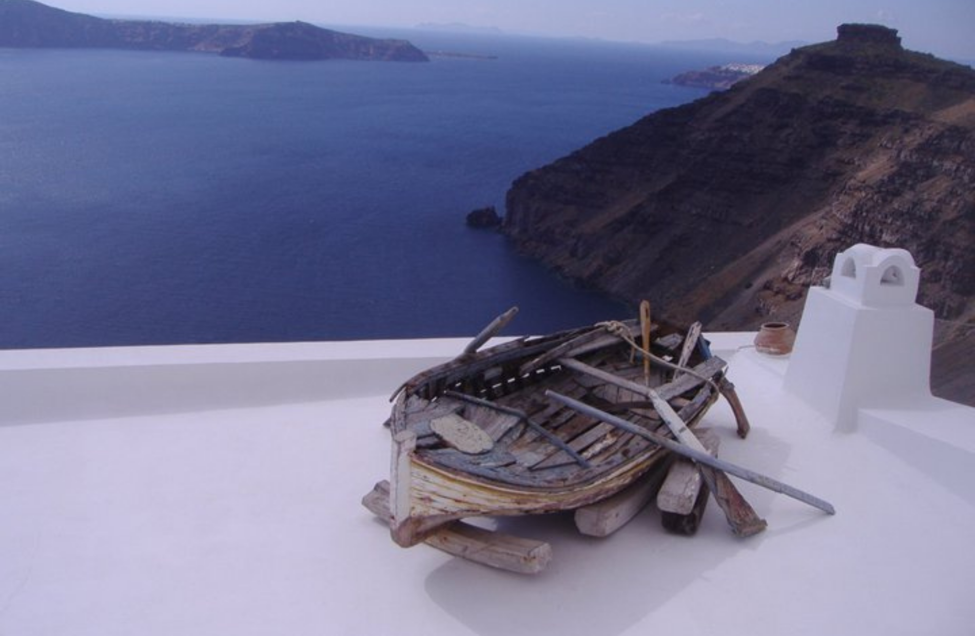 an ancient wooden boat on the top of a white roof overseeing the sea and mountainside in the background