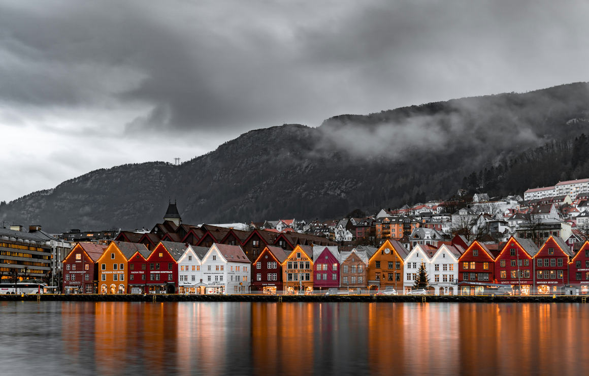 colorful wooden houses along the Bryggen Wharf in Bergen under a cloudy sky and mountains behind