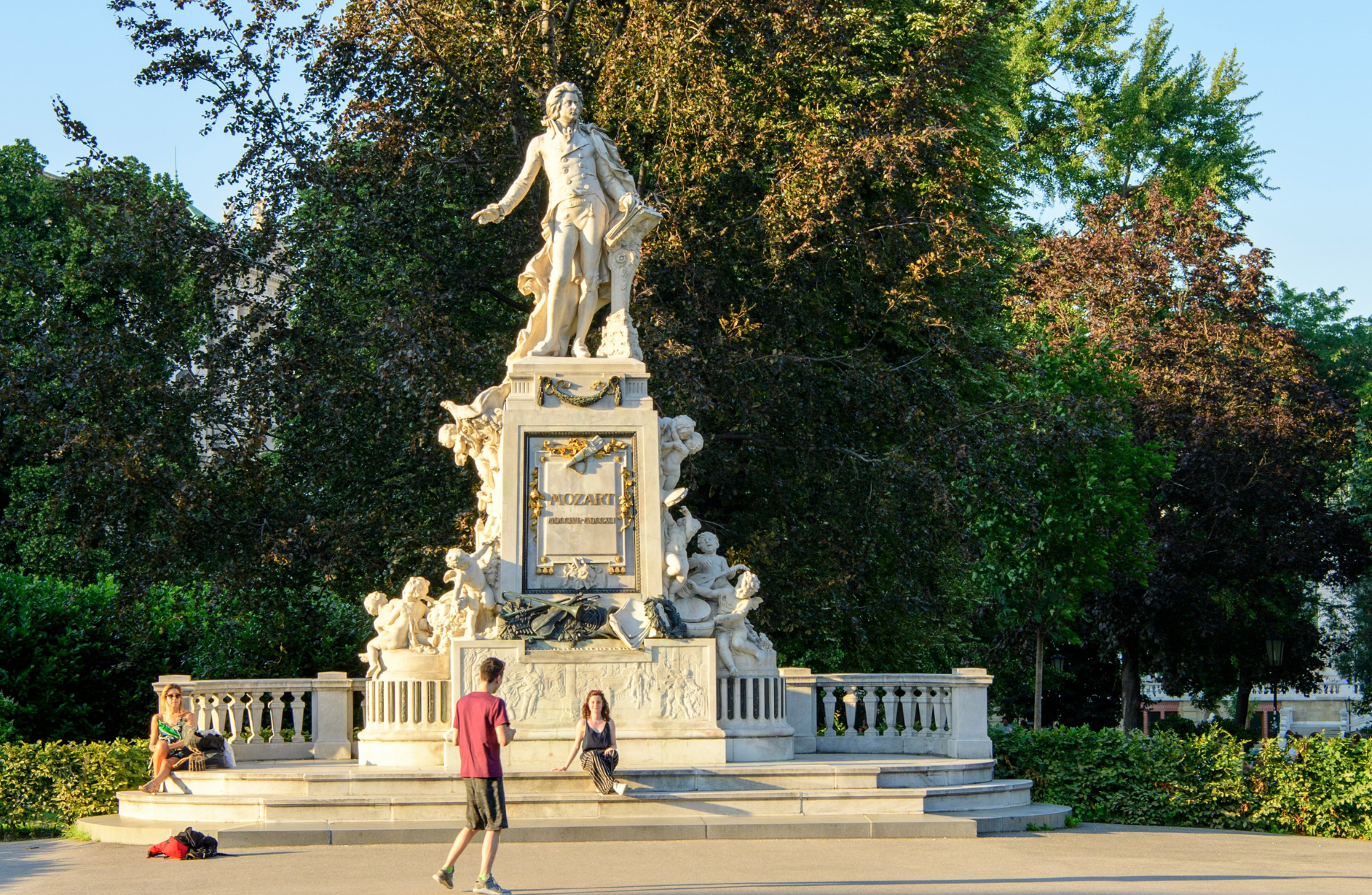 people sitting in front of status of Mozart in park during daytime