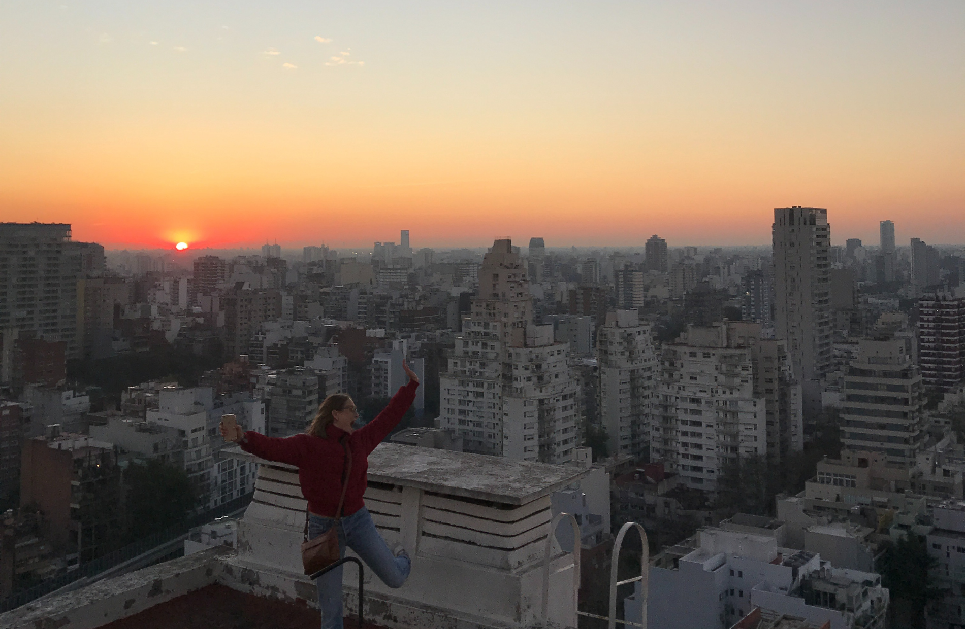 woman jumping with glee on a roof top with the sunset in the backgroung