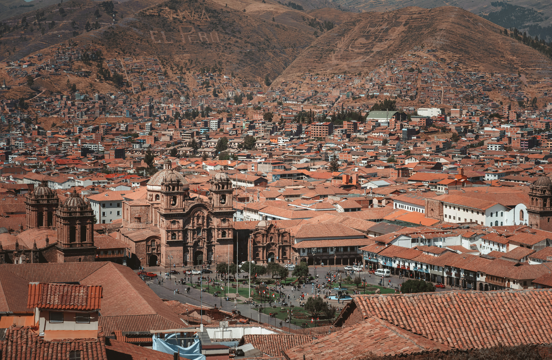 sprawling view of the red roof tops and a cathedral in the center, with the words El Peru on the mountainside in the background