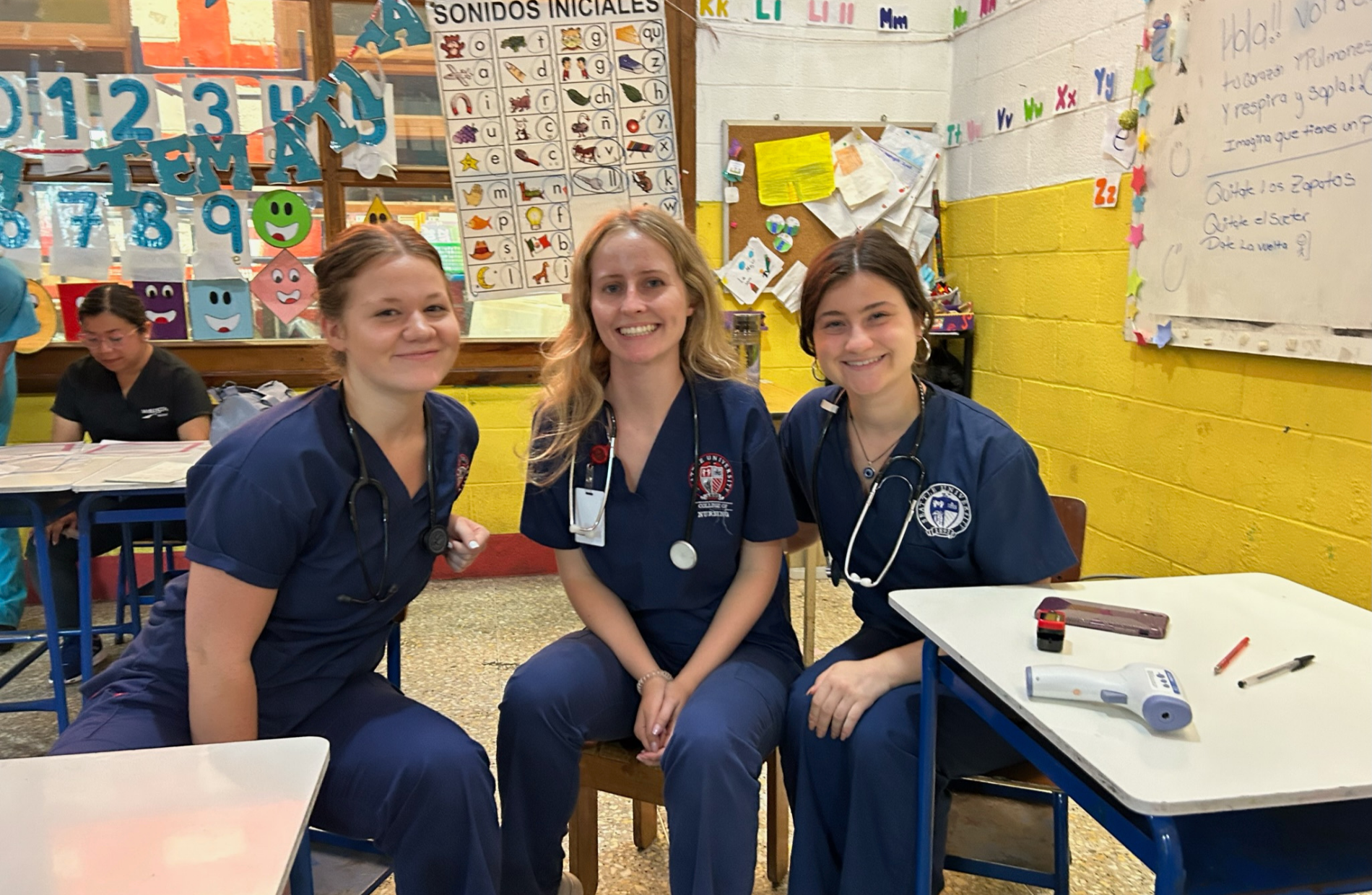 three nursing students smiling in a Guatemalan elementary school classroom