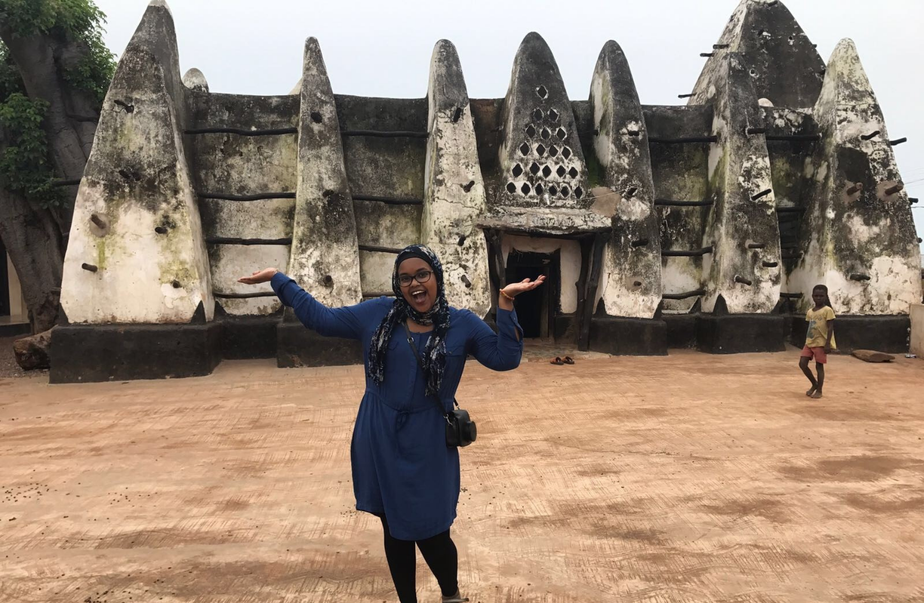 smiling woman with their hands up in front of a Ghanies historical building