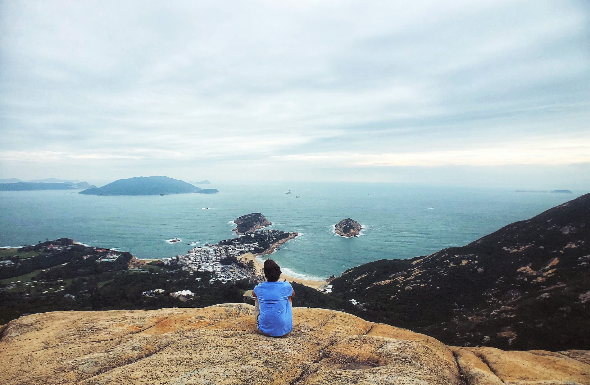 a man sitting on a cliffside overlooking a small peninsula lined with homes