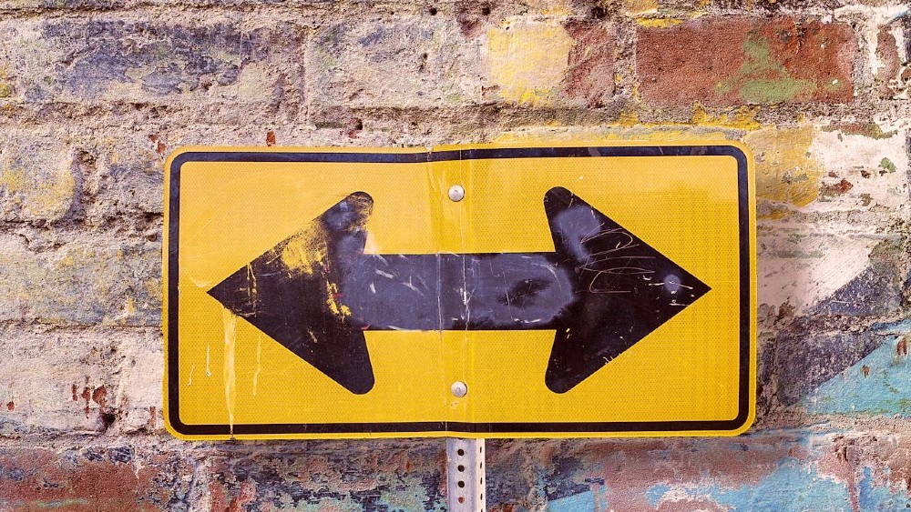 Photo of a two-way arrow street sign against a brick wall