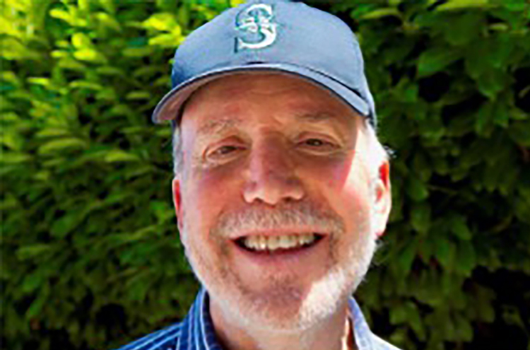 Lane Gerber smiling in front of greenery with Mariner's hat