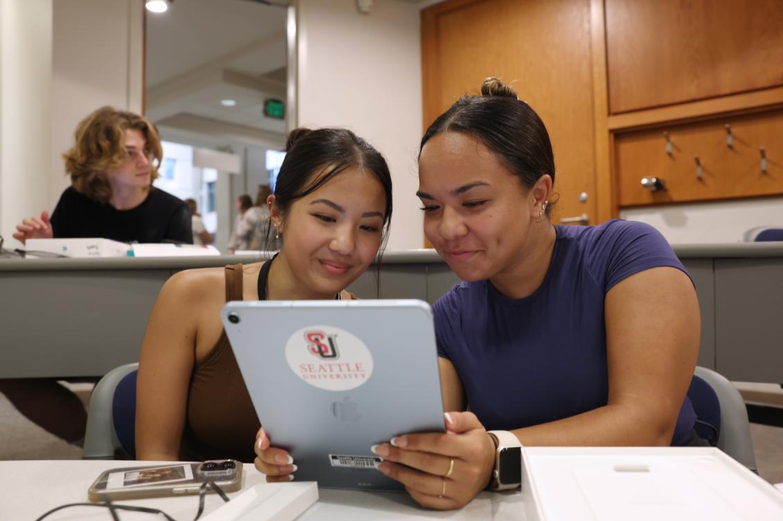 2 students sitting next to each other sharing an ipad