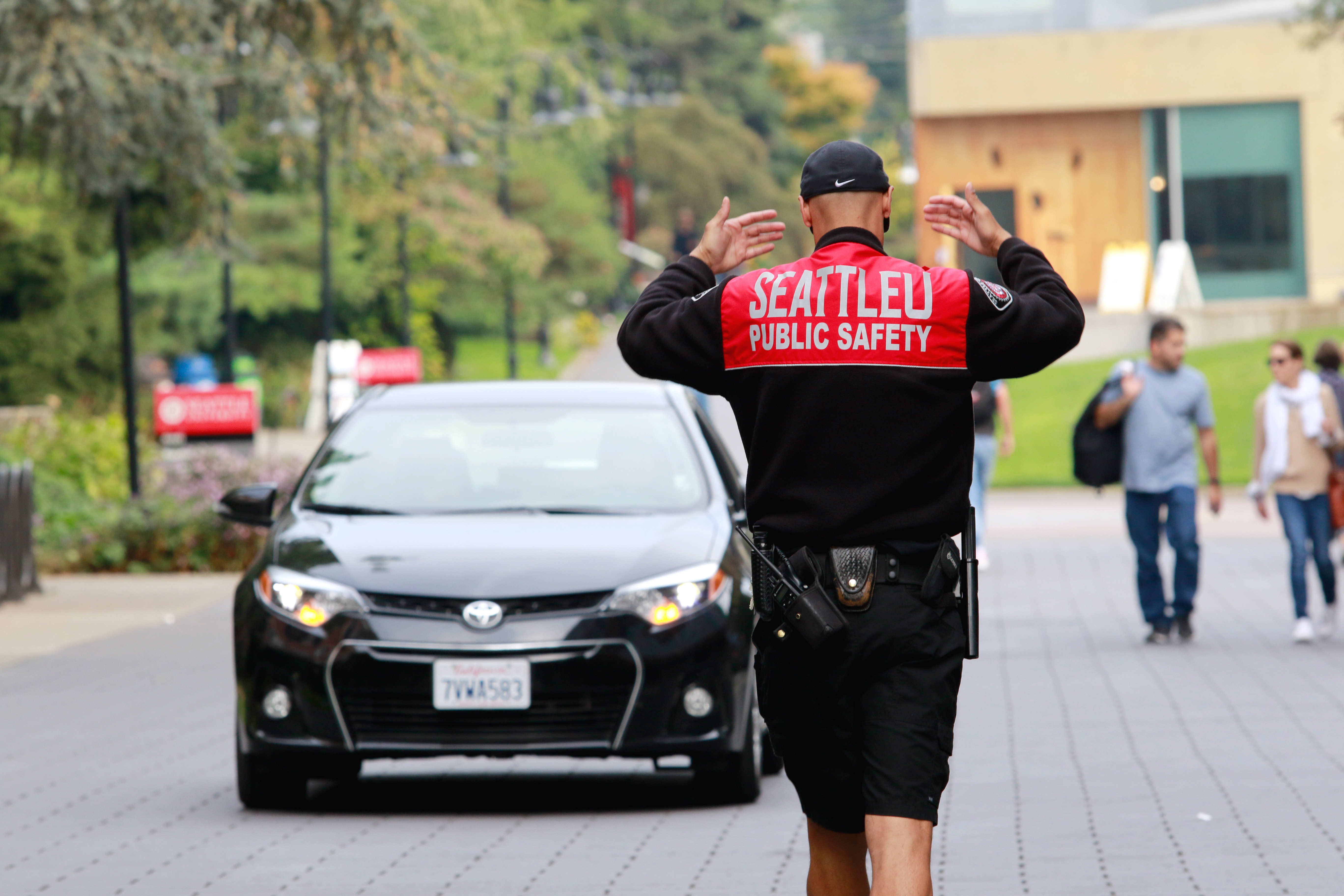 DPS officer directing traffic with both arms up. Back facing camera. A black sedan is driving toward the officer.