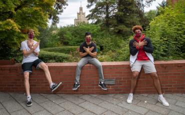 A photo of three male basketball athletes on campus wearing masks and forming their hands into the Redhakw symbol