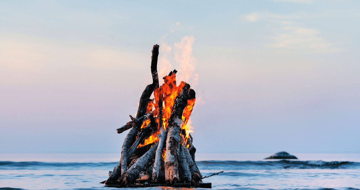 An image of a bonfire burning during daylight on a beach.