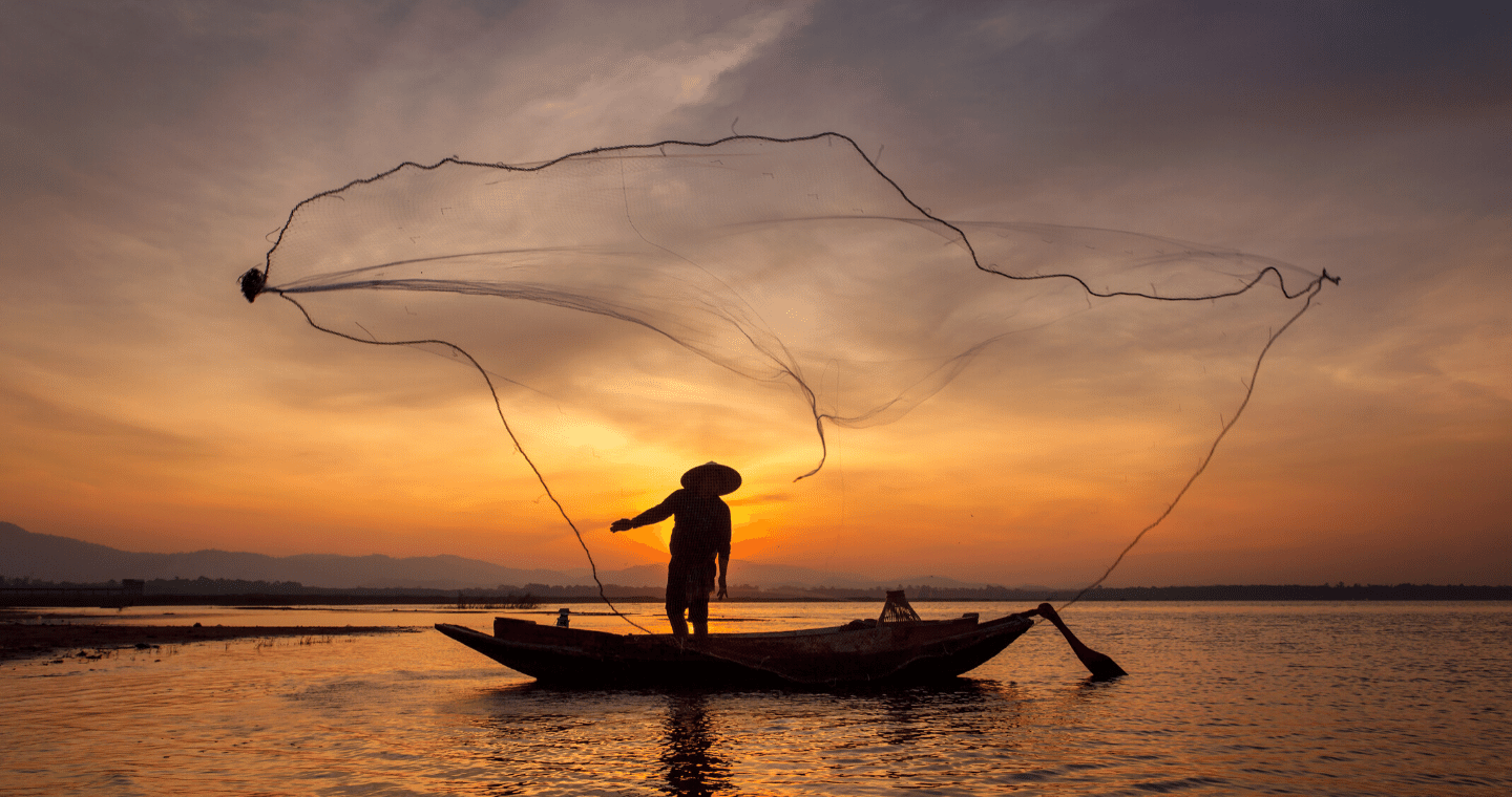 A person in a fishing boat at sunset casts a net.