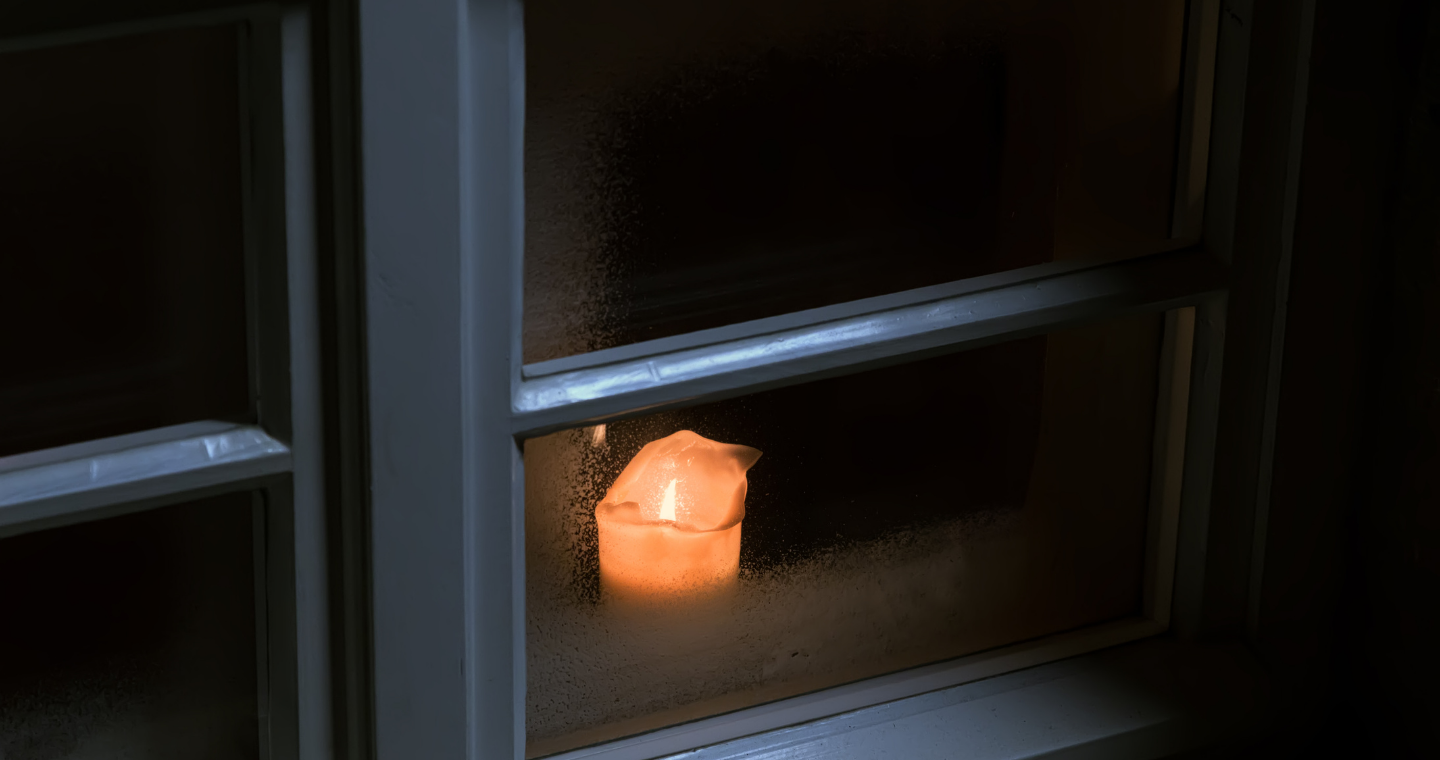a lit candle burns in a dark window