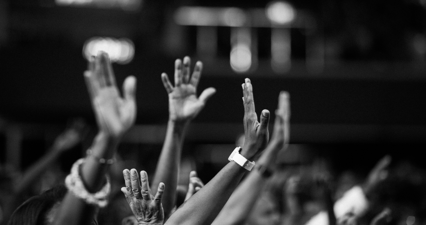 black and white photo of group praying with raised hands in prayer
