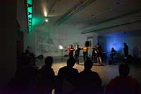 Performers dancing in Vachon Gallery with green and blue lights and video projection