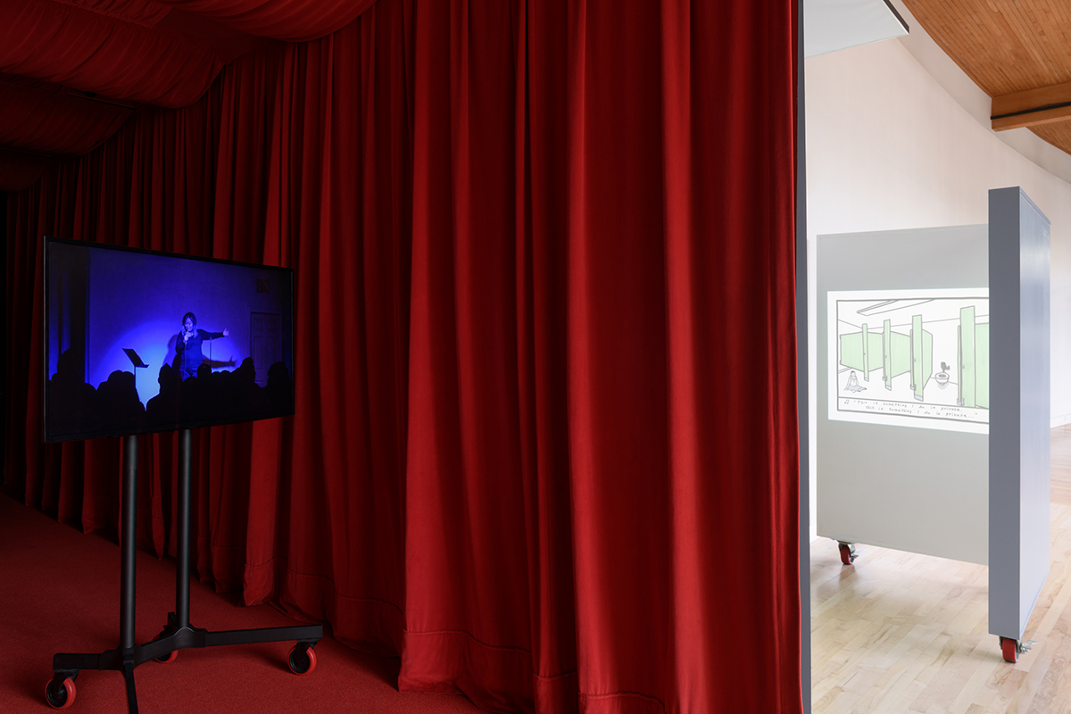 View of art gallery, Tv monitor in hallway with red curtain beside cubicle with video projection inside