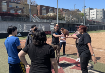 A professor handing a blow-up kiwi bird to the winning team of a kickball game.