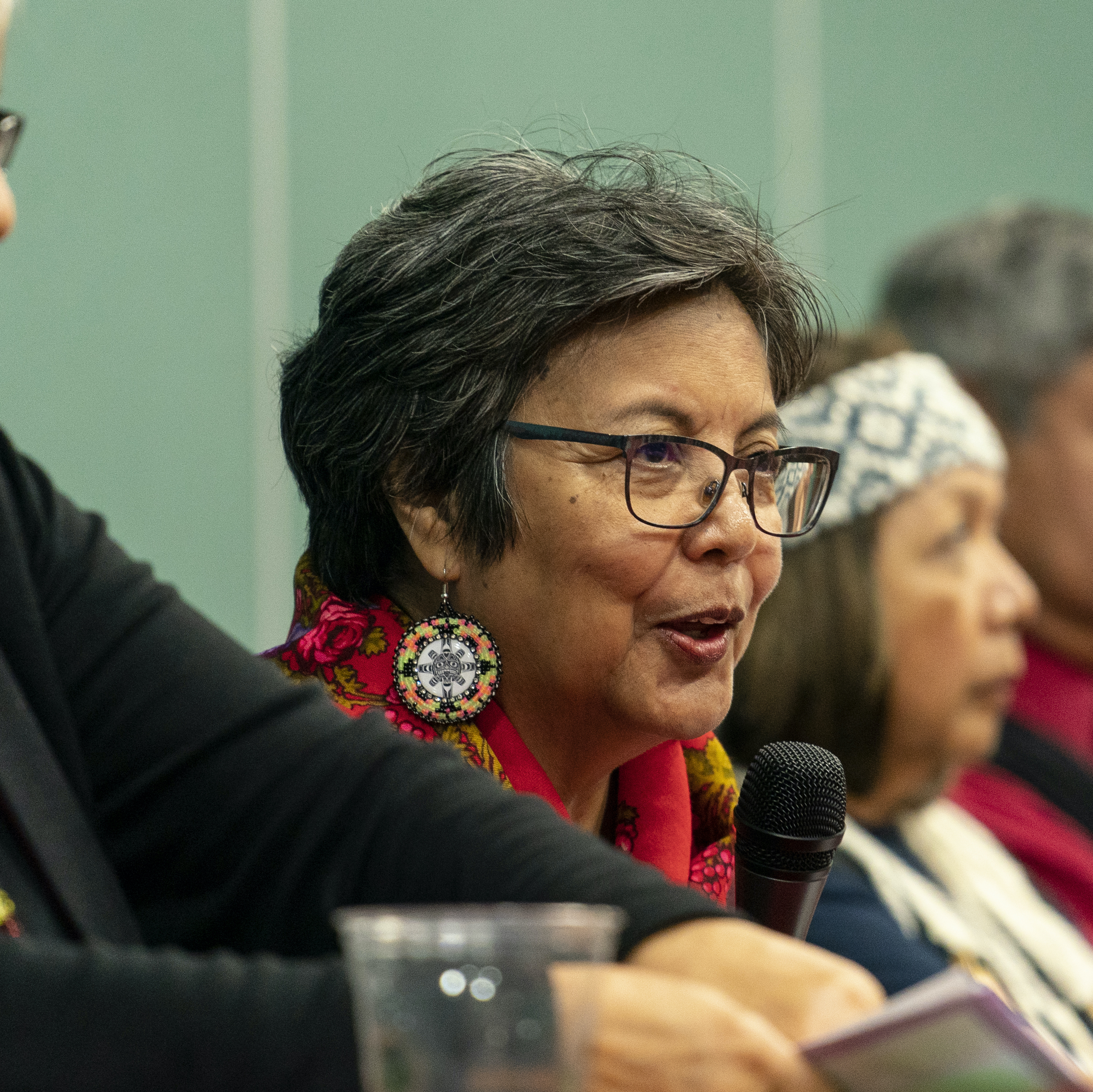 women in glasses and beaded earrings talking into a microphone
