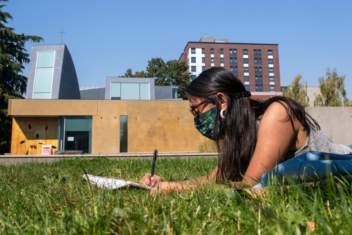 Student in a mask studying in the grass