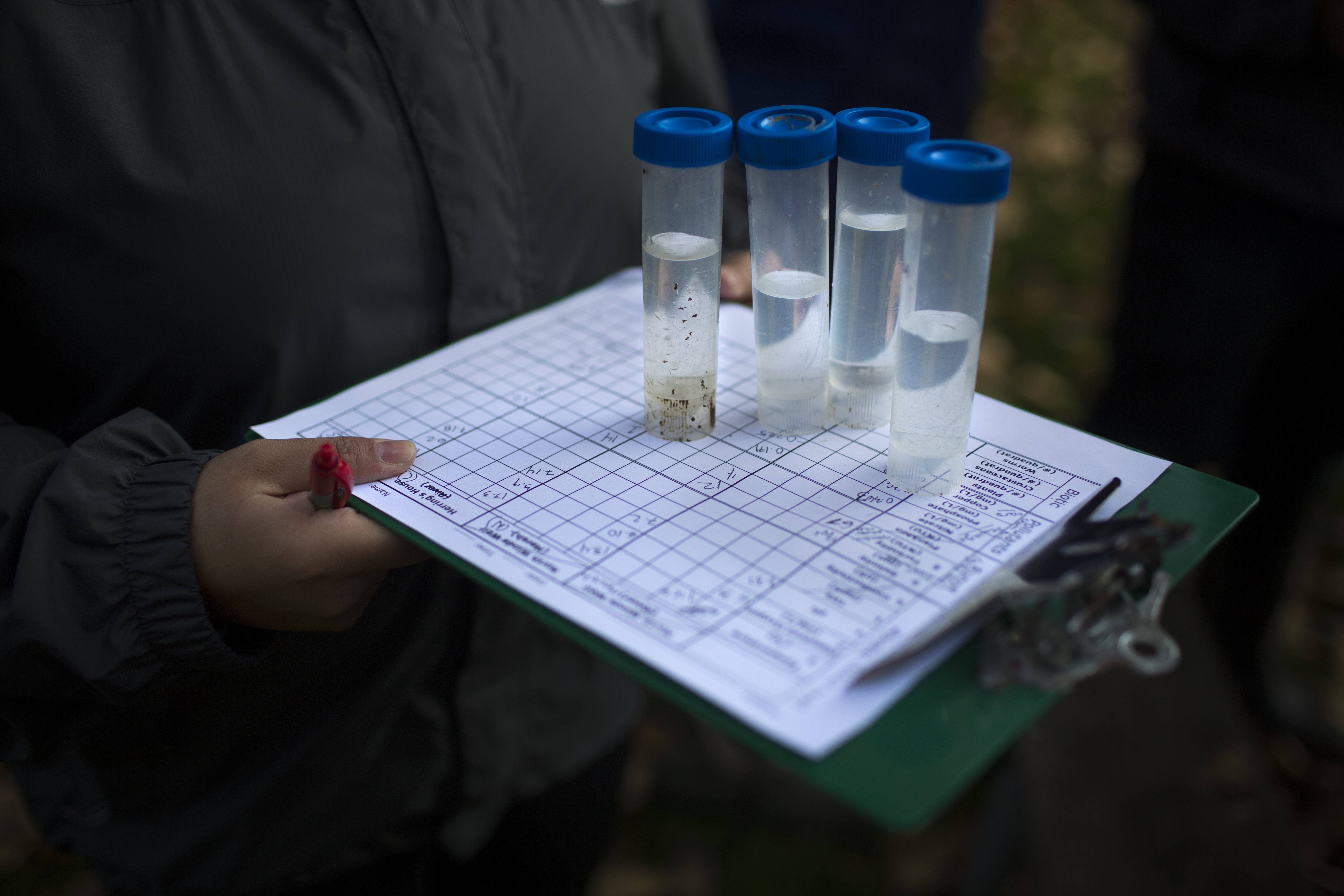 Student holds a green clipboard with vials of samples from the Duwamish River.
