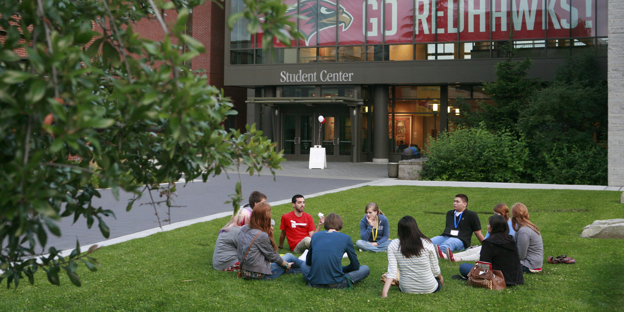 a group of students sitting in a circle on the lawn in front of the Student Center