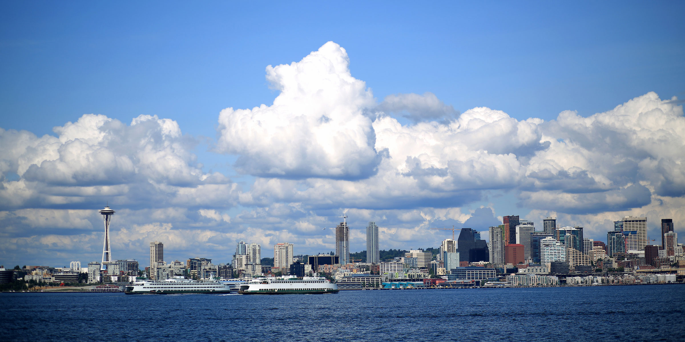view of blue skies and puffy white clouds above the Seattle skyline and waterfront from Alki Beach in West Seattle
