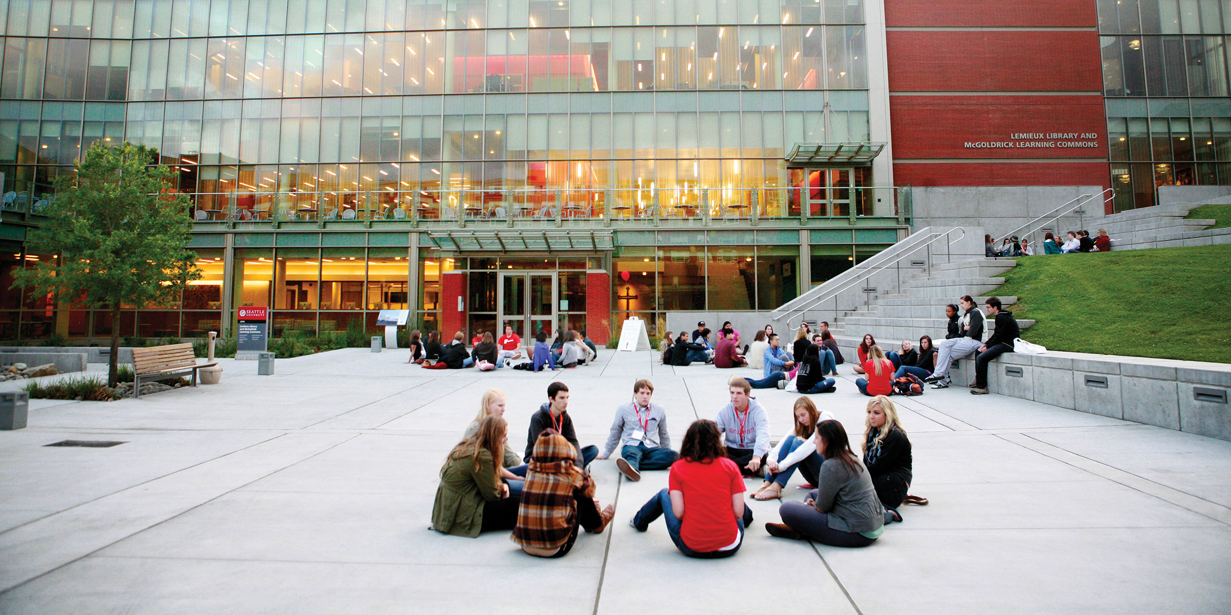 a group of students talk and sit in a circle in the Lemieux Library plaza