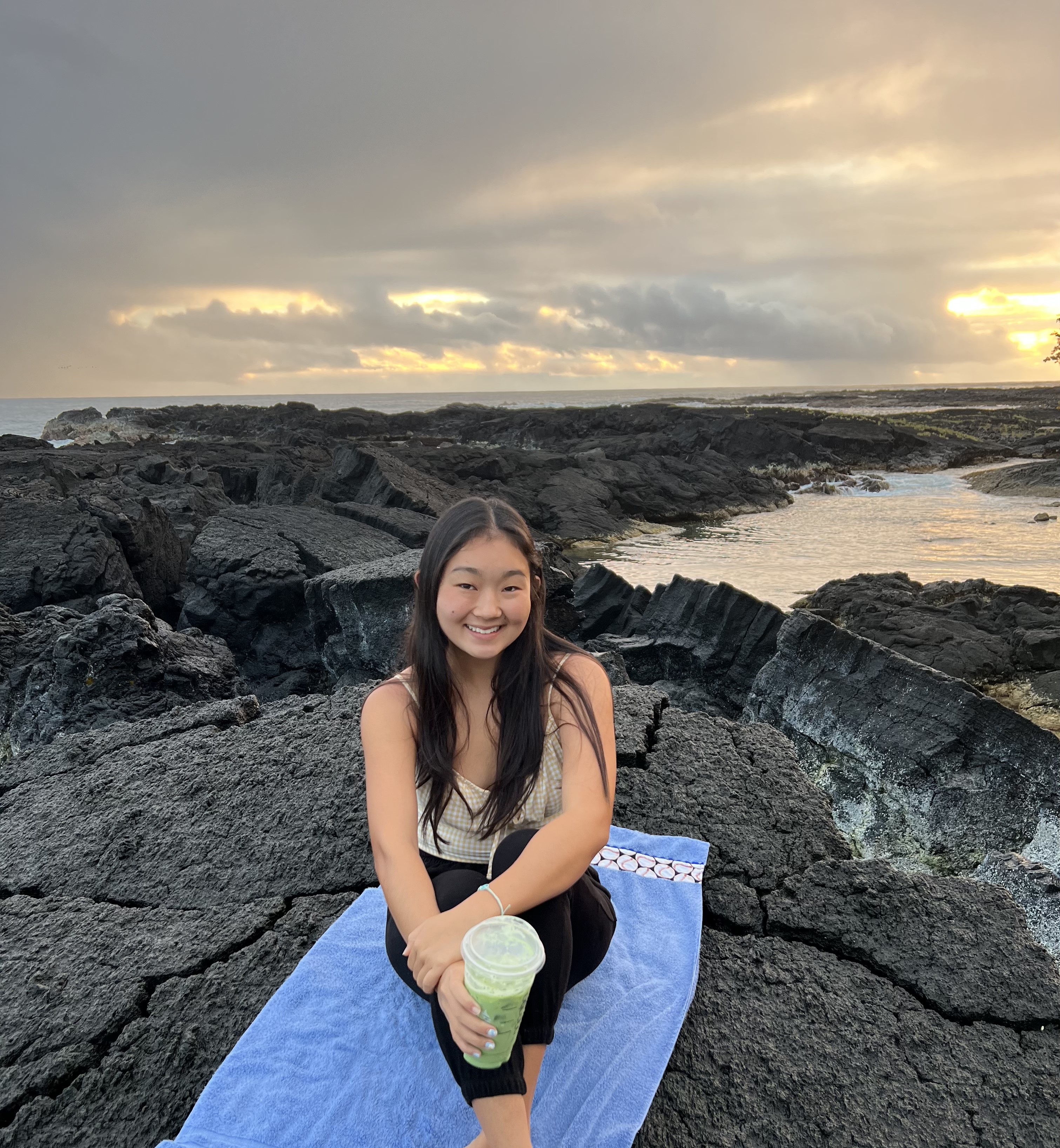 Student photographed sitting on a rock with ocean in the background