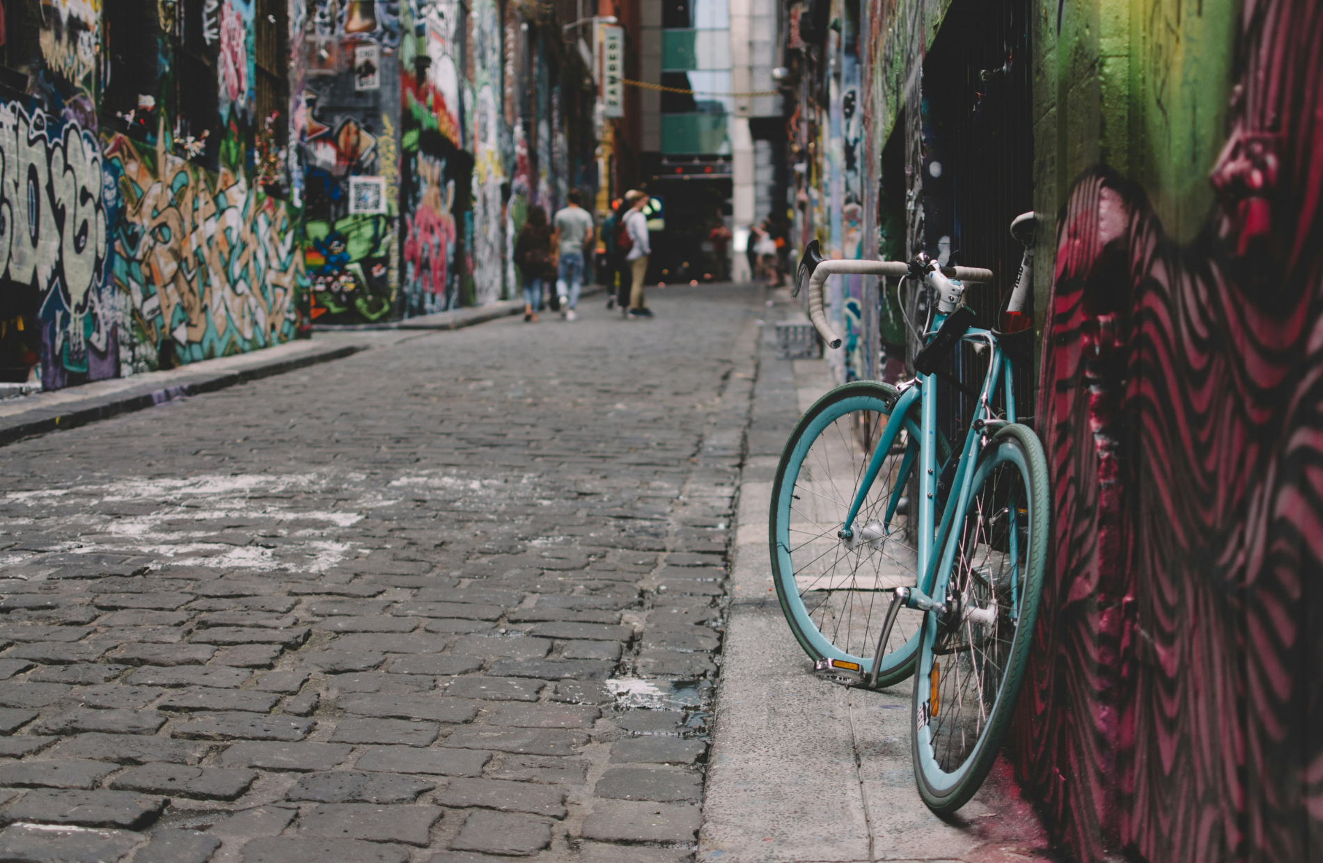 a bicycle leaning on the side of a building along a cobble street lined with graffitied walls