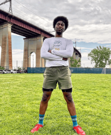 A young athlete posing with arms crossed in a field by a bridge