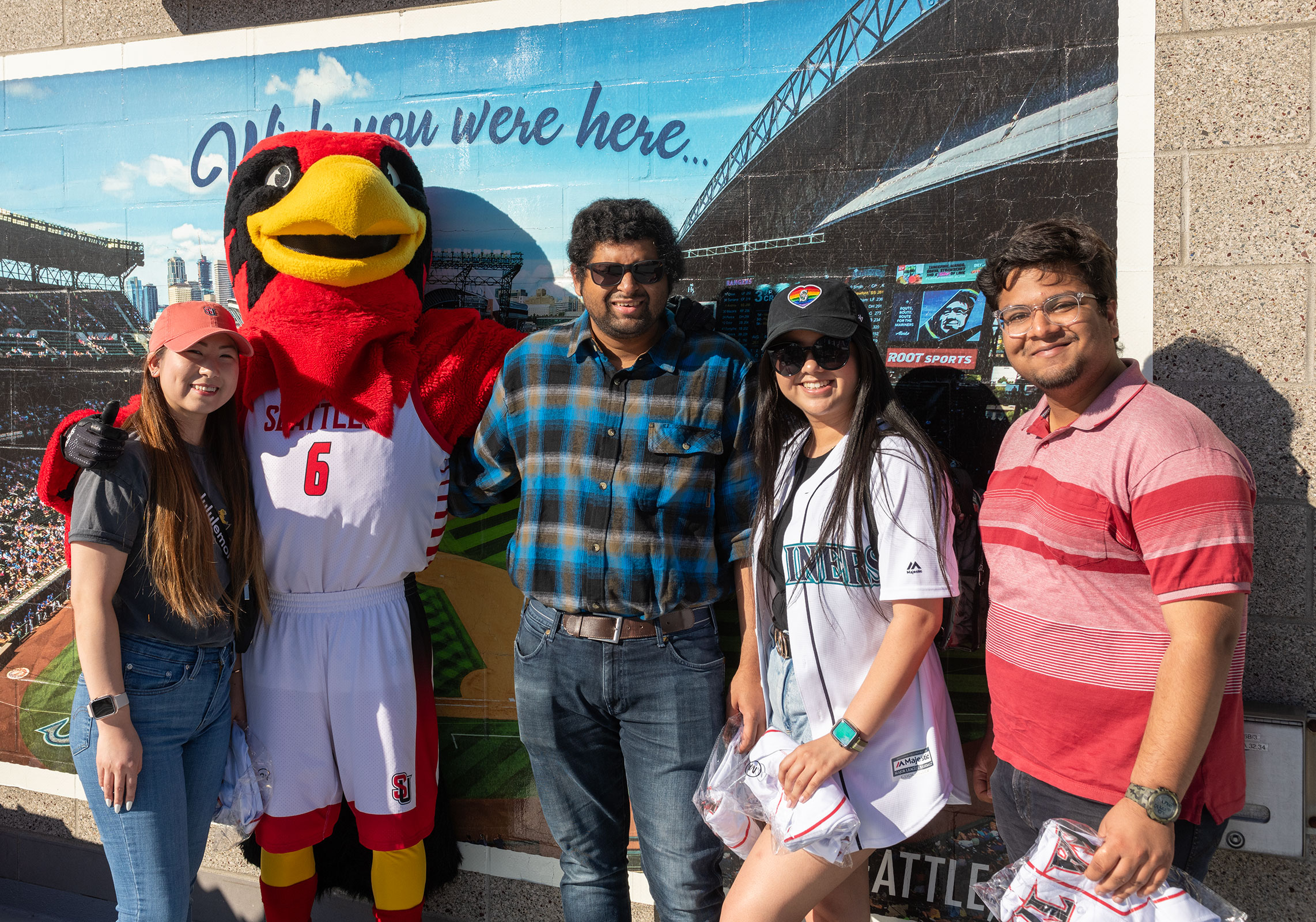 4 students and Rudy posing in front of Mariners sign