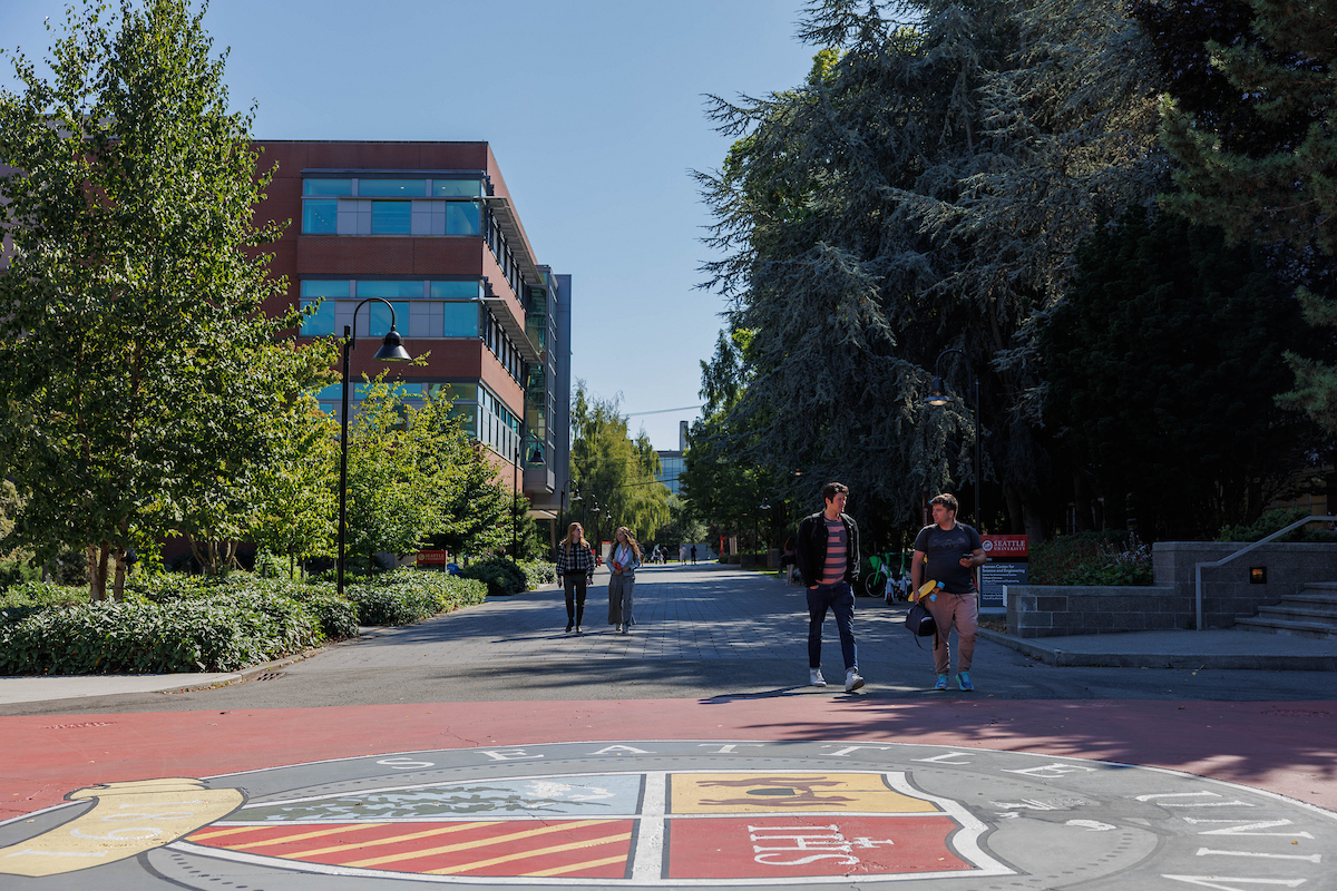 students walking on the lower mall with the school seal in the foreground