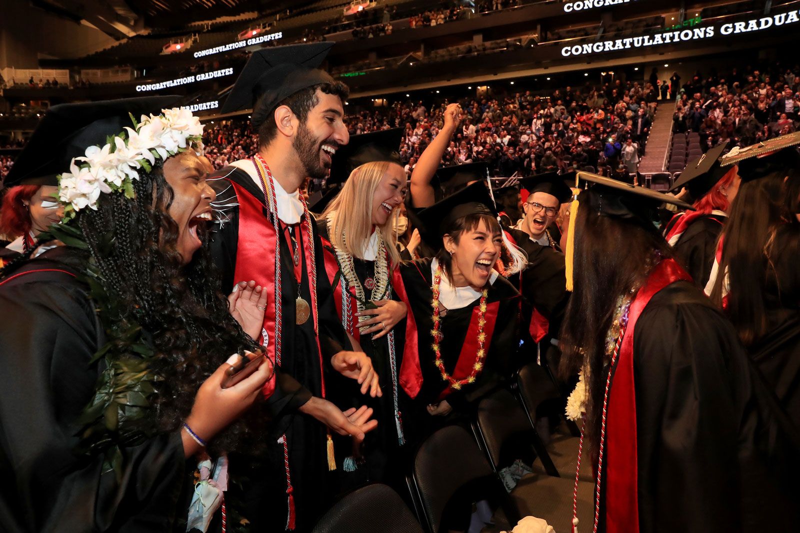 A group of grads in regalia, smiling, clapping and cheering excitedly inside Seattle's Climate Pledge Arena.