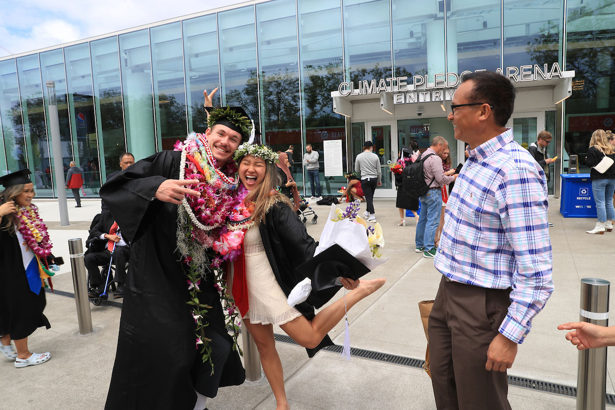 Grads pose for pictures in festive regalia outside the Climate Pledge Arena in Seattle