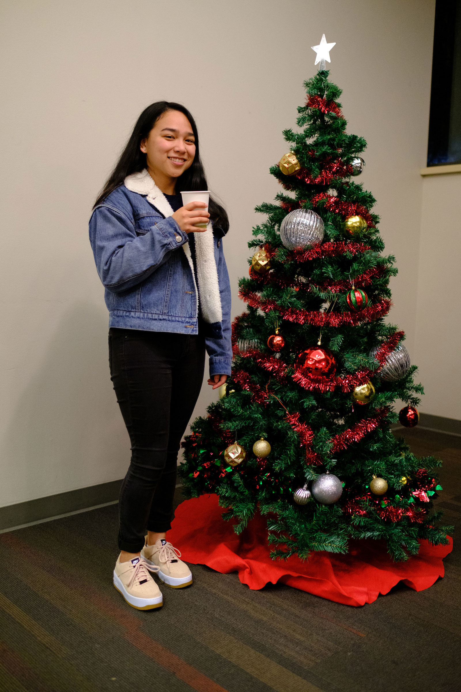 a student poses for a camera shot with a decorated Christmas Tree in the student center