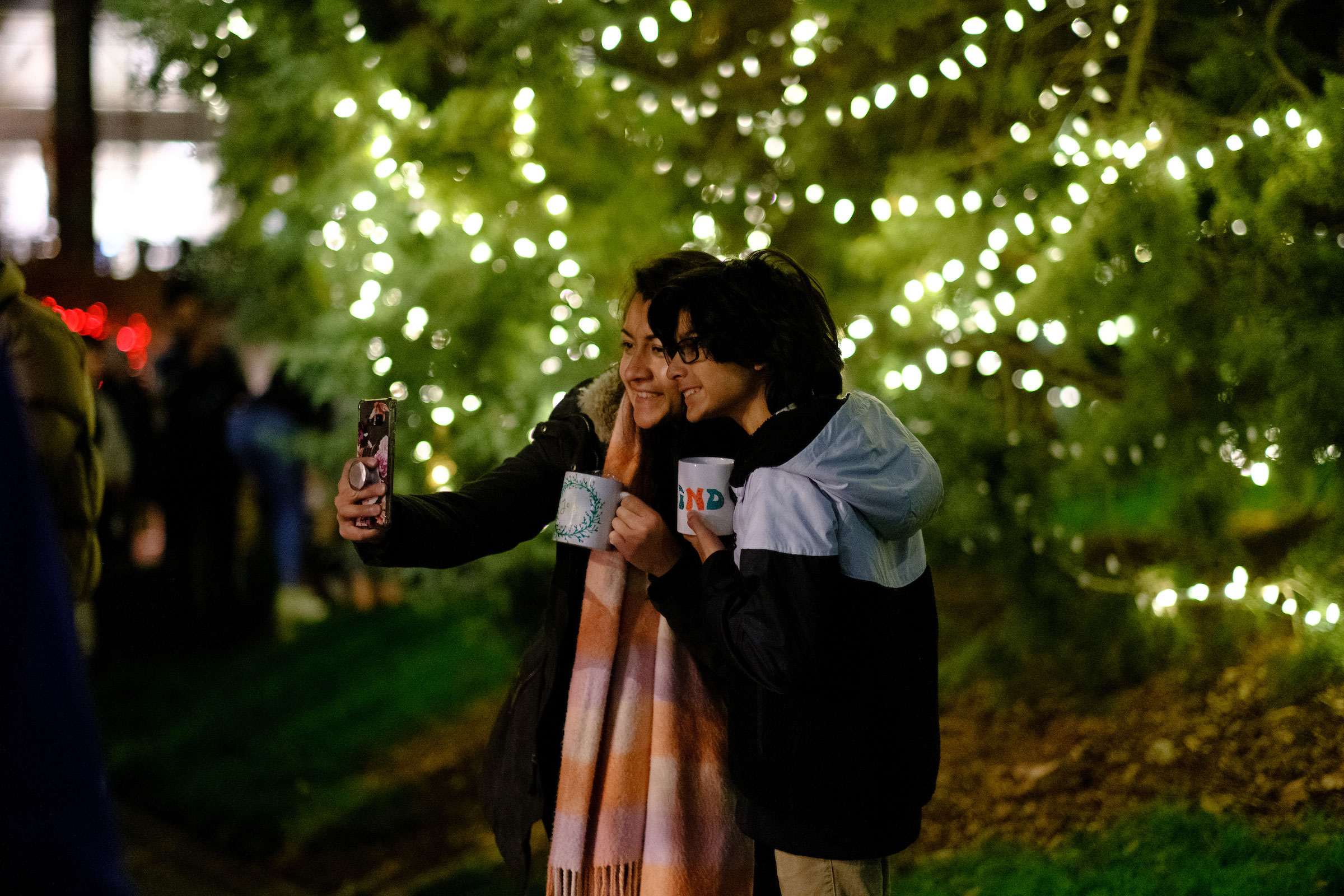 two students pose for a group selfie in front of the campus Christmas Tree