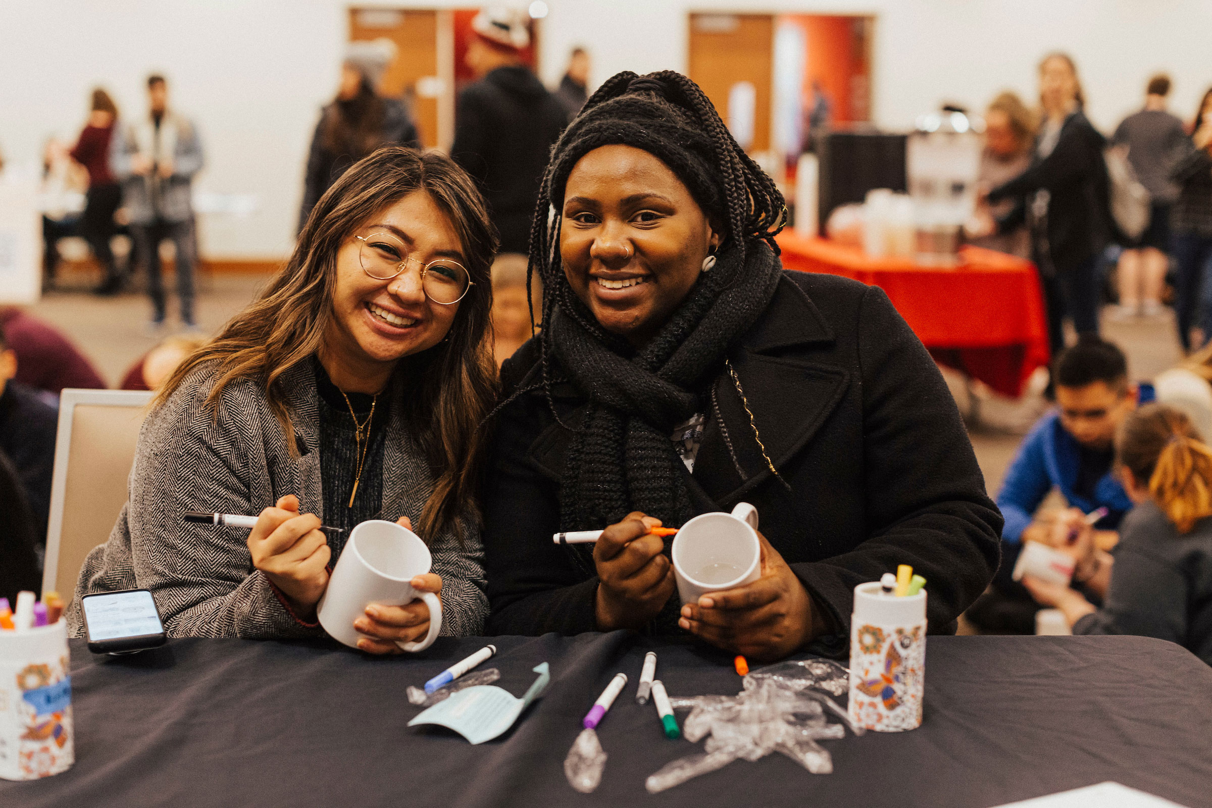 two students pose for a shot while decorating mugs