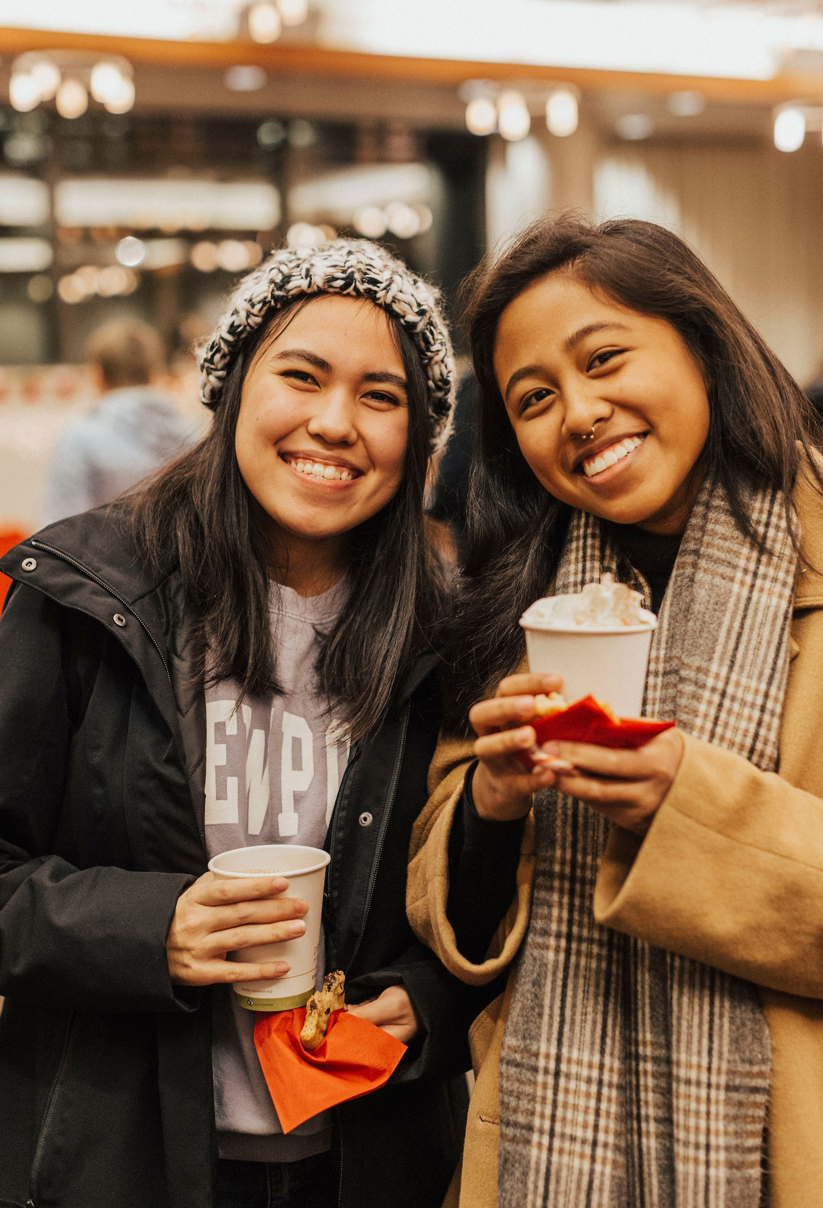 two students smile holding warm festive beverages