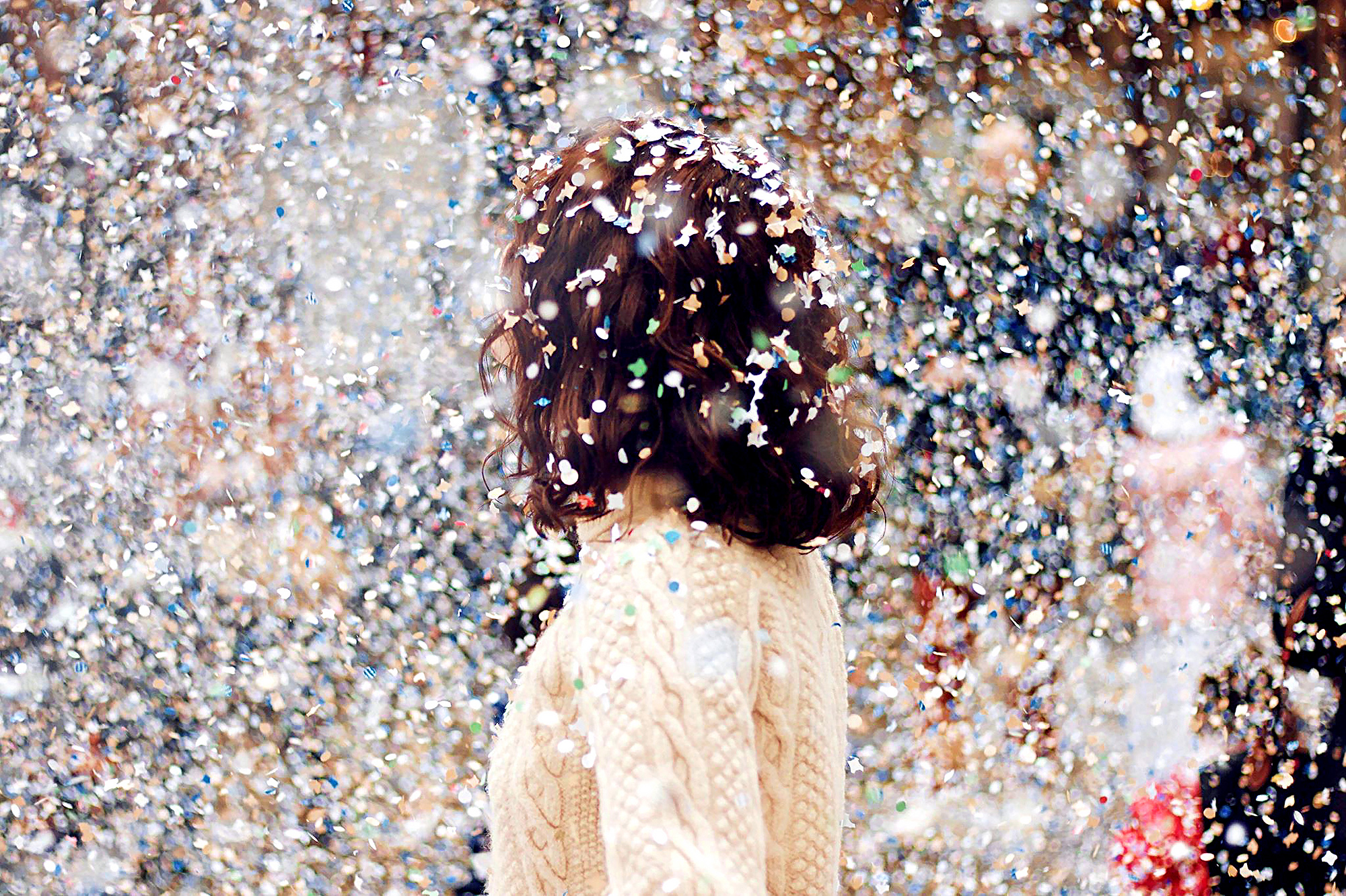 a woman with long brown hair stands amidst a flurry of multi-colored confetti