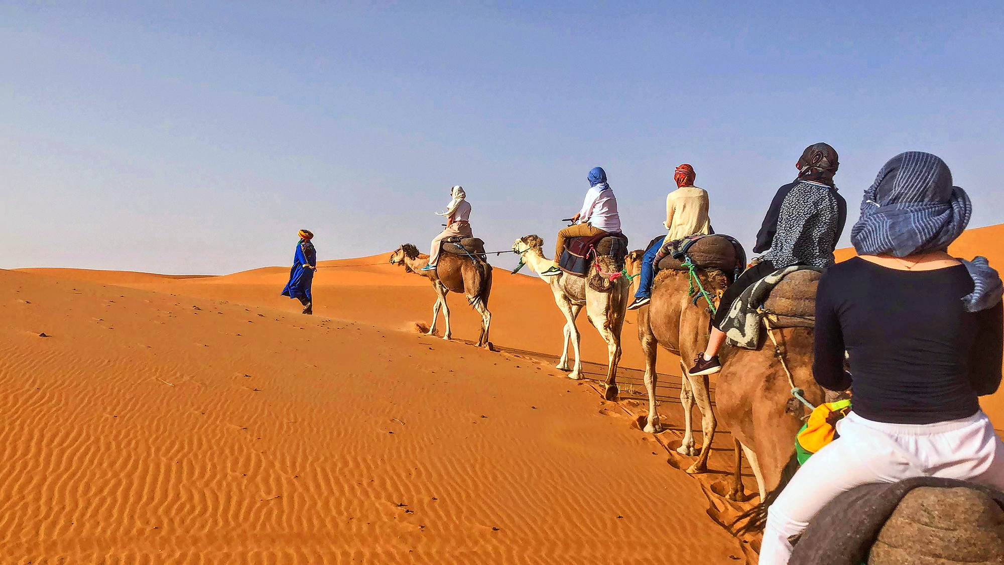 caravan of travelers riding camels in the Moroccan desert