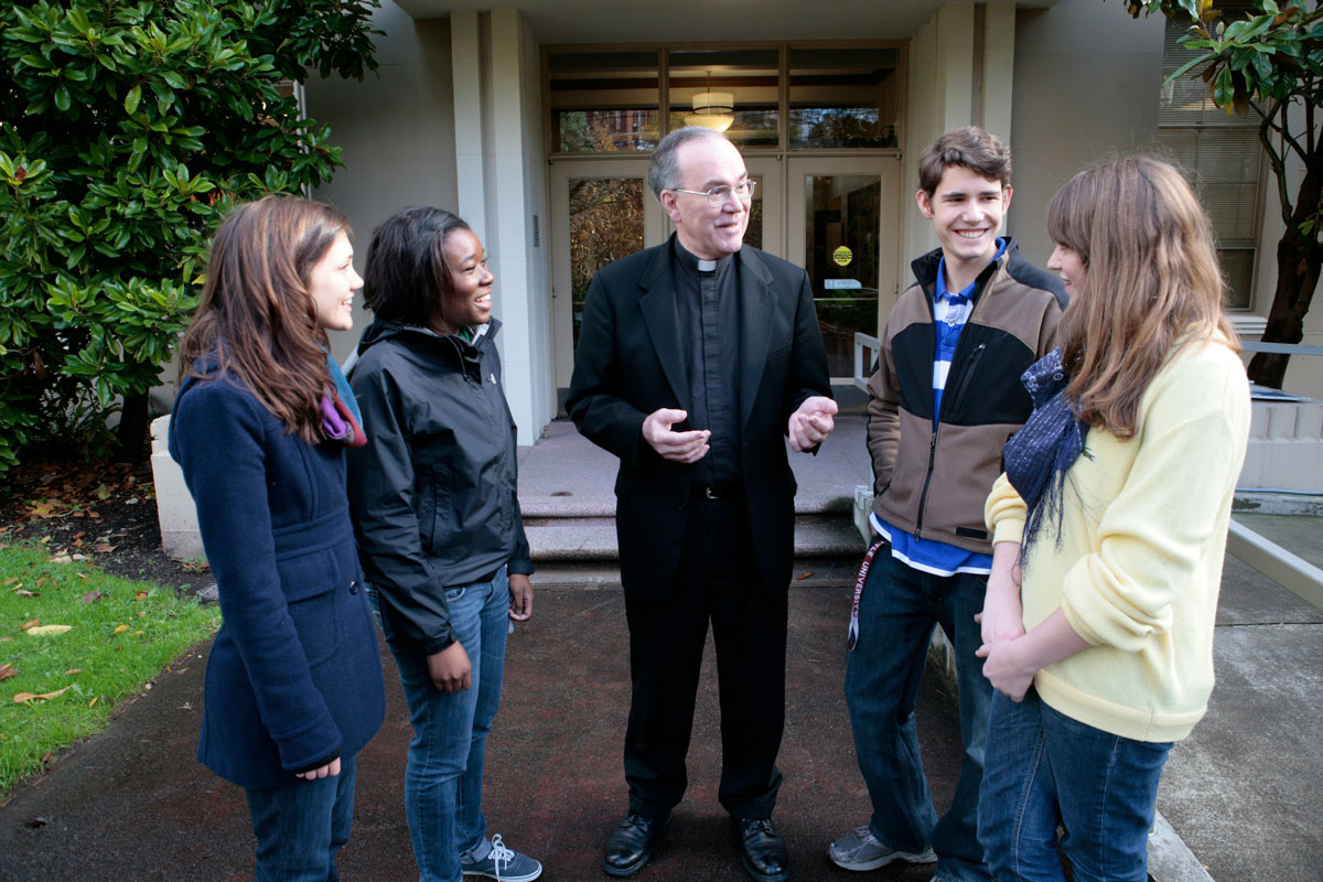 Father Sundborg standing in conversation with students on campus
