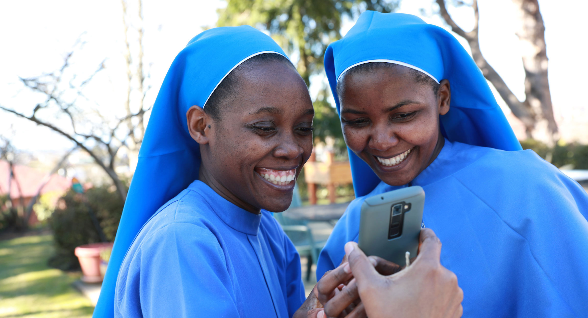 Sister Mary Namutebi, DM, '20, '22, left and Sister Paskazia Ampronia Nakitende, DM, '19 with The Daughters of Mary Sisters in Uganda share a moment together while reviewing a selfie photo they took on their cell phone in the garden at their St. Joseph's Residence in West Seattle. 